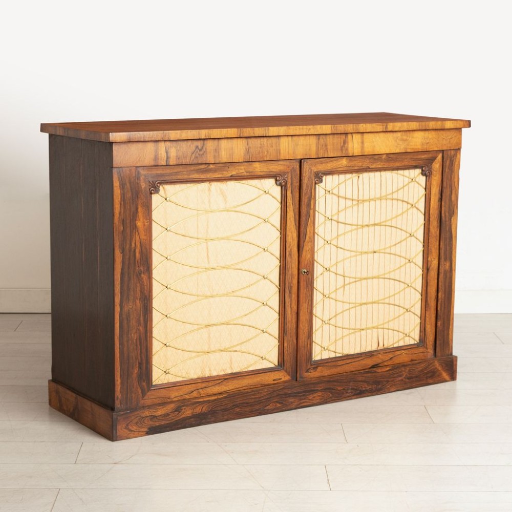 An antique mid-nineteenth century rosewood side cabinet featuring two doors with brass wire grilles over pleated fabric panels and a plinth base. View II