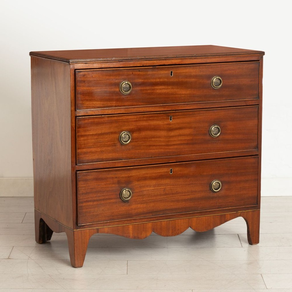 A Georgian mahogany chest of three long drawers featuring brass ring handles, escutcheons, and a scalloped apron resting on bracket feet. View II