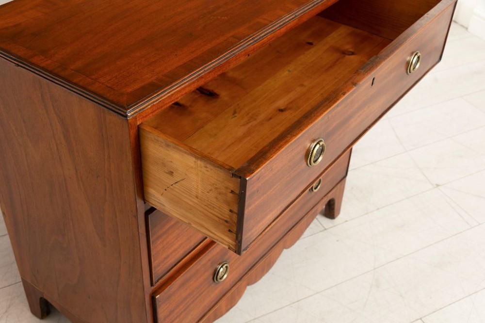 A Georgian mahogany chest of three long drawers featuring brass ring handles, escutcheons, and a scalloped apron resting on bracket feet. View IV