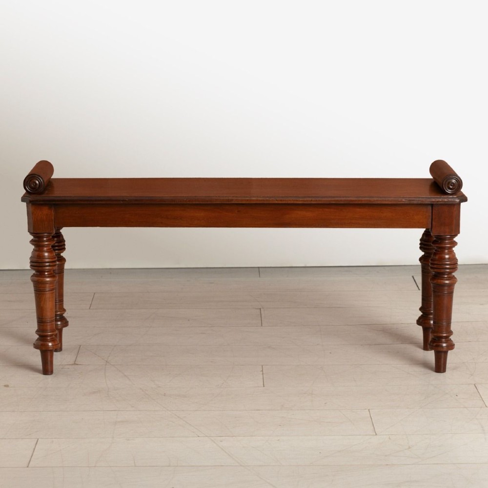 A nineteenth-century Victorian solid mahogany window seat featuring a flat rectangular top, rolled scroll bolsters at either side, and four turned legs. View II