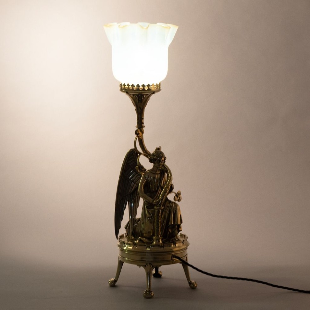 A late Victorian Gothic Revival brass table lamp featuring a detailed kneeling angel figure supporting a frilled vaseline glass shade. View II