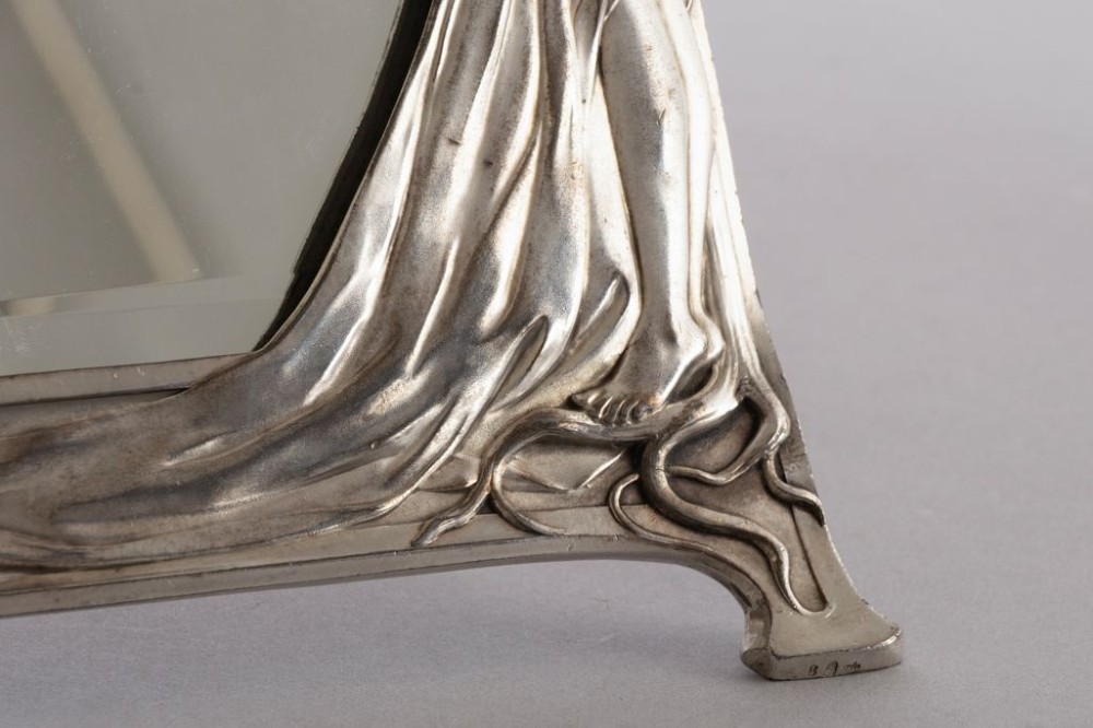 An Art Nouveau pewter easel-backed mirror featuring a sculptured maiden figure and relief floral motifs around a rectangular glass frame. View II
