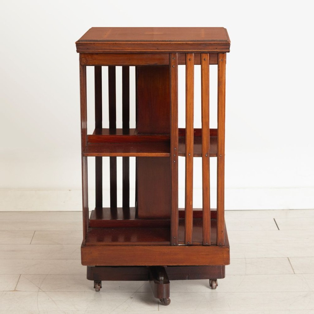 An Edwardian mahogany revolving bookcase featuring two tiers with vertical slatted sides, central rotating mechanism, and a quadruped base on castors. View II