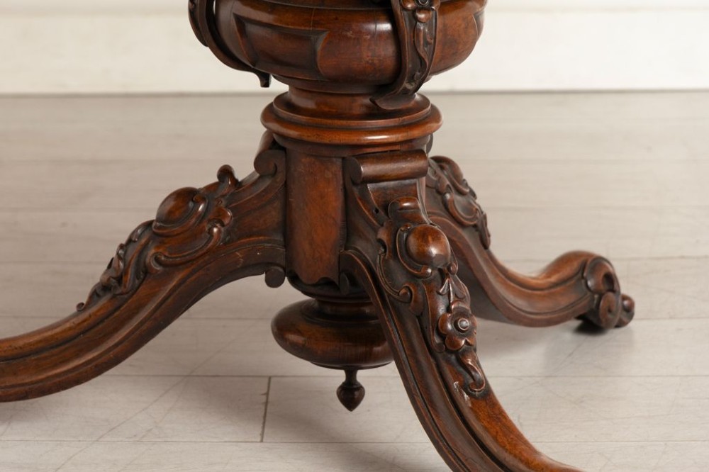 A Victorian rosewood tilt-top dining table featuring an oval top with a scalloped apron, supported on a carved pedestal column with scroll tripod legs. View III