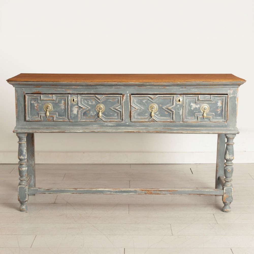 An antique oak dresser base featuring a natural wooden top, distressed grey painted finish, geometric moulded drawers with brass handles, and turned legs with a lower stretcher.