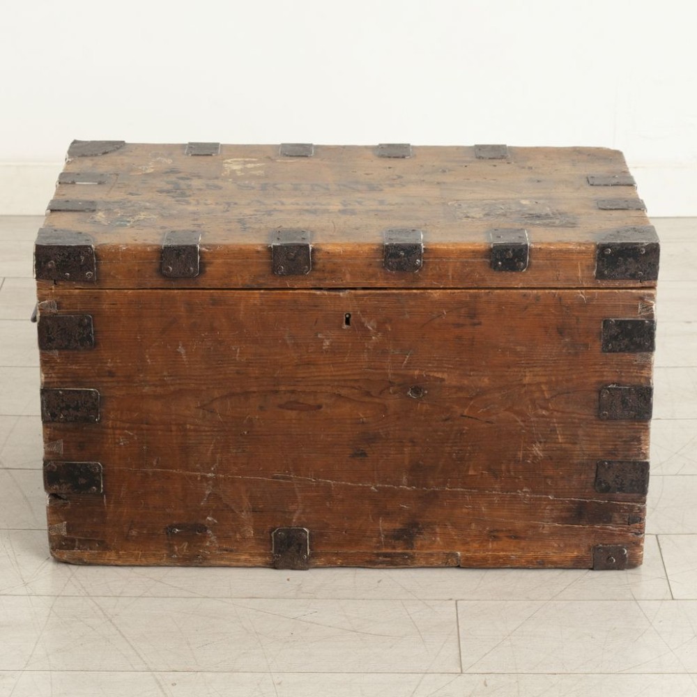A rectangular Victorian pine travel trunk featuring iron corner straps, a front keyhole, and stencilled black text across the top lid.