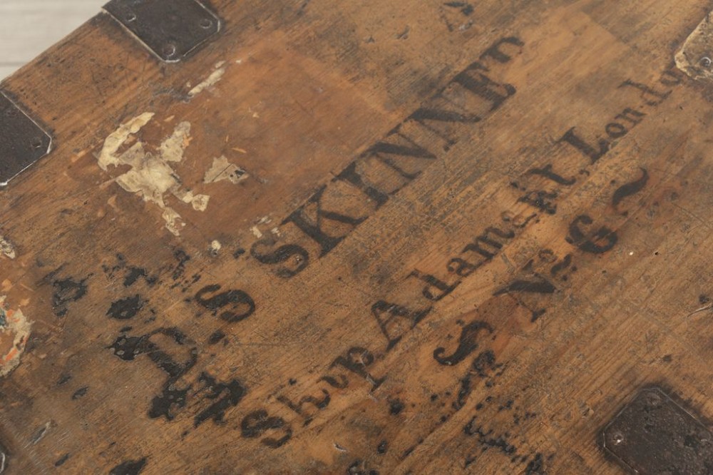 A rectangular Victorian pine travel trunk featuring iron corner straps, a front keyhole, and stencilled black text across the top lid. View IV