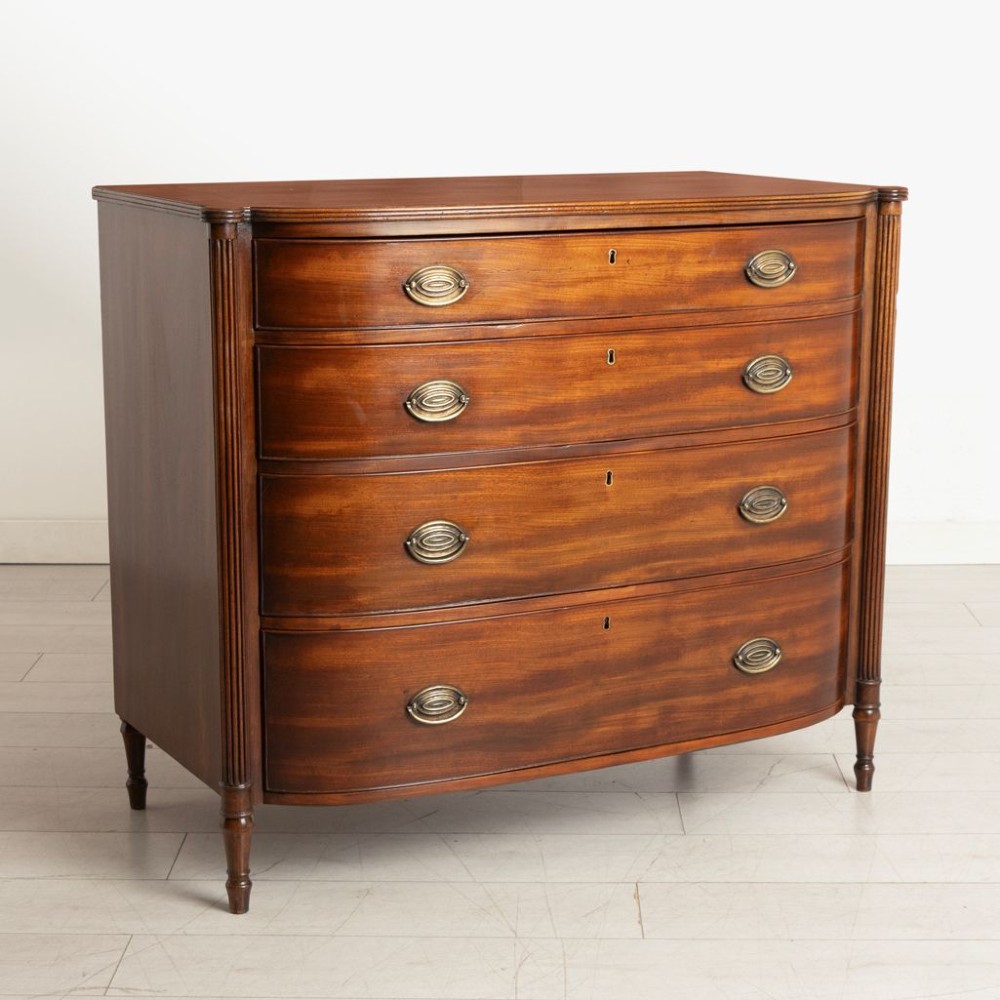 A Regency period mahogany bow-fronted chest featuring four graduated drawers with brass oval handles and reeded side columns. View II