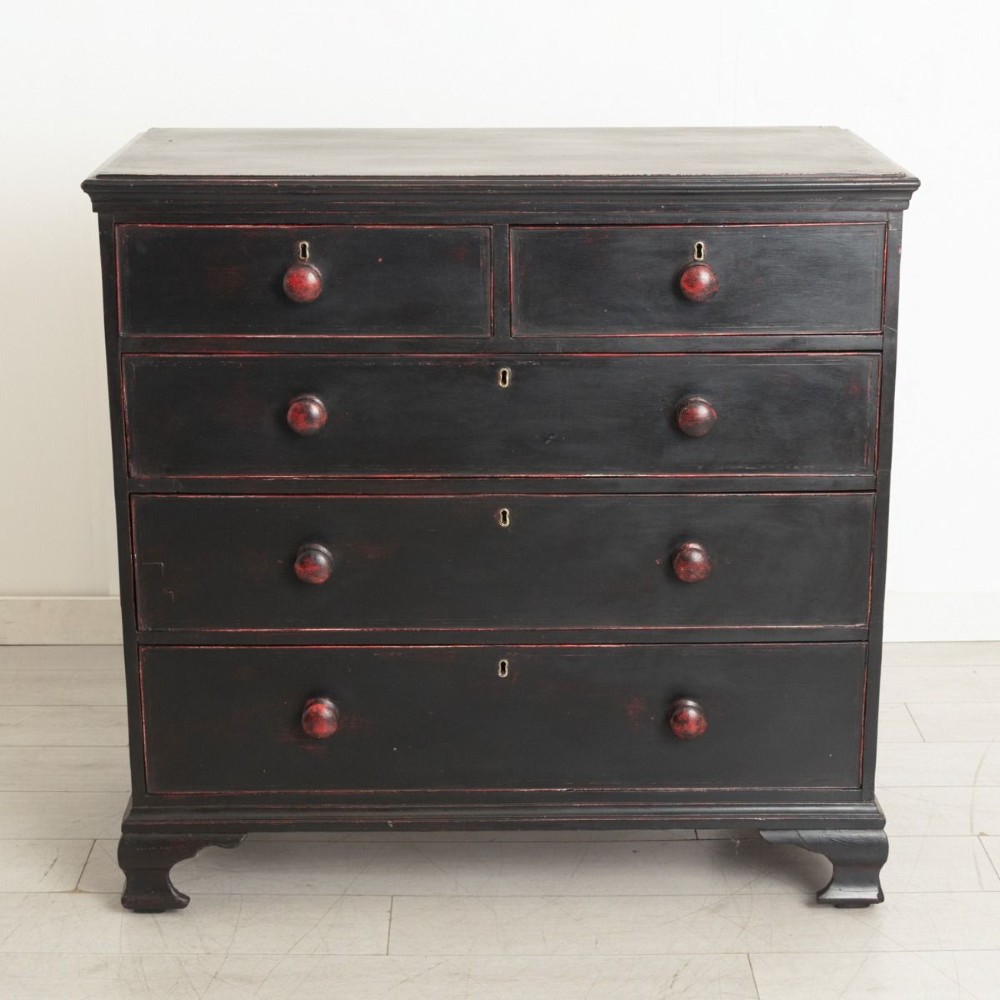 A 19th-century two-over-three chest of drawers with a distressed black painted finish over red undercoats, featuring turned wooden knobs and brass escutcheons.