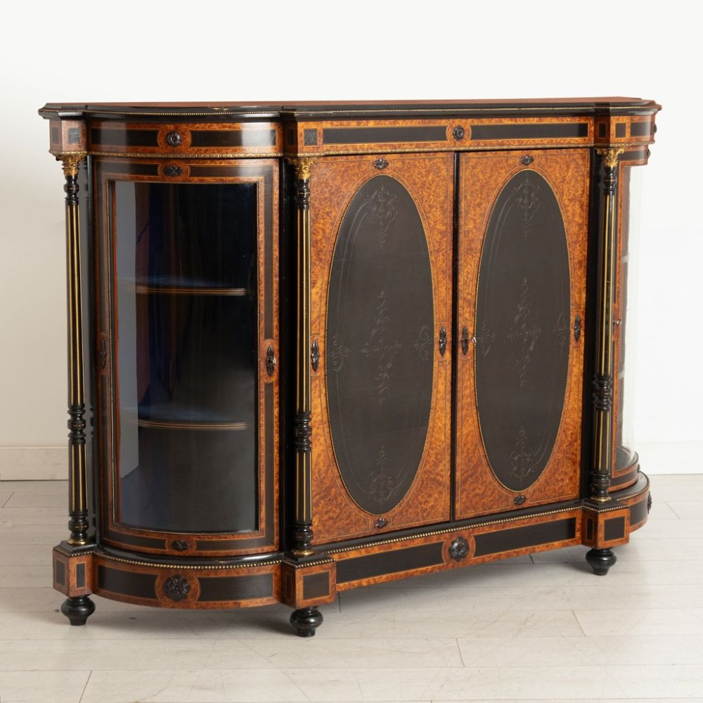 An early Victorian credenza crafted in figure-grained amboyna wood with ebony borders, featuring two central oval-panelled doors flanked by curved glazed side doors and gilt column accents. View II