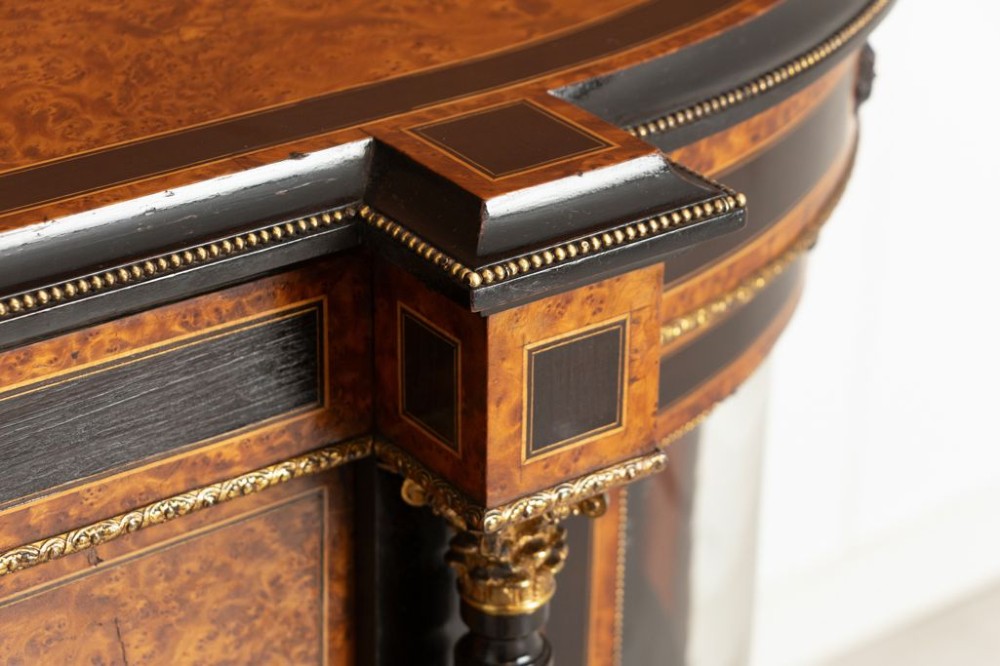 An early Victorian credenza crafted in figure-grained amboyna wood with ebony borders, featuring two central oval-panelled doors flanked by curved glazed side doors and gilt column accents. View V