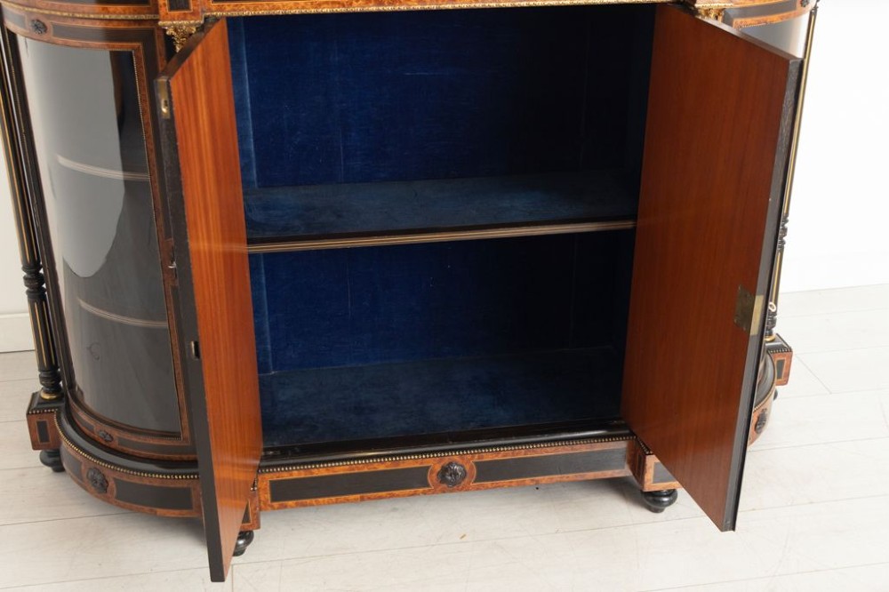 An early Victorian credenza crafted in figure-grained amboyna wood with ebony borders, featuring two central oval-panelled doors flanked by curved glazed side doors and gilt column accents. View VI