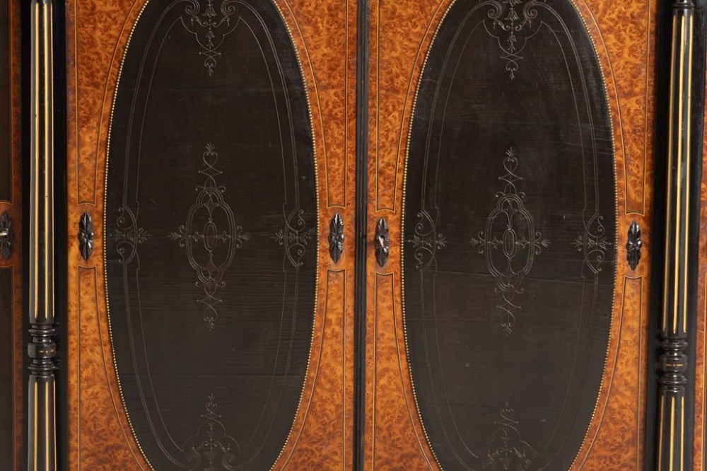 An early Victorian credenza crafted in figure-grained amboyna wood with ebony borders, featuring two central oval-panelled doors flanked by curved glazed side doors and gilt column accents. View VII