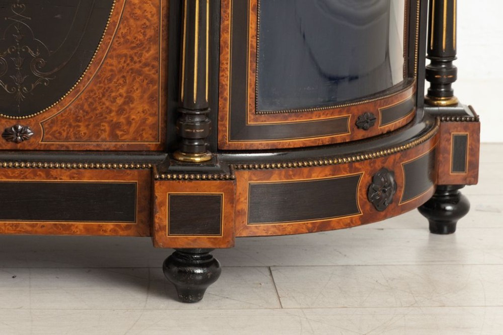 An early Victorian credenza crafted in figure-grained amboyna wood with ebony borders, featuring two central oval-panelled doors flanked by curved glazed side doors and gilt column accents. View VIII