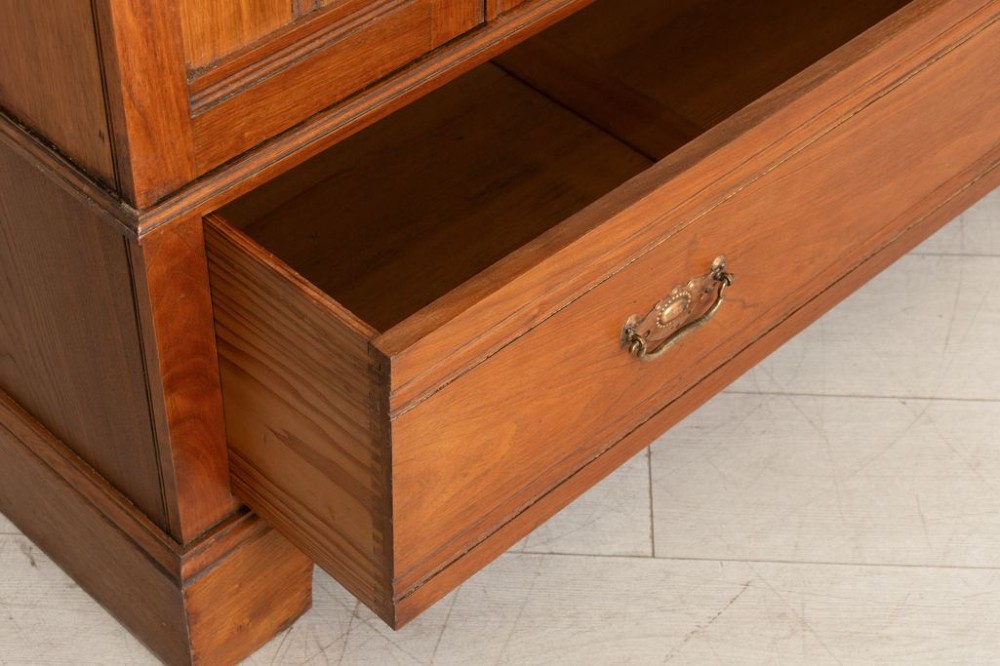 A tall Arts and Crafts walnut wardrobe featuring a central mirrored door flanked by carved timber panels above a single base drawer. View IV