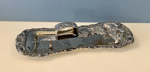 fig 1. An antique silver-plated scissor-style candle snuffer with a central box resting beside a matching oblong tray decorated with engraved floral motifs and scroll borders.