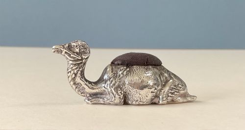 fig 1. An antique silver novelty pin cushion cast in the form of a seated camel with a dark fabric cushion integrated into its back.