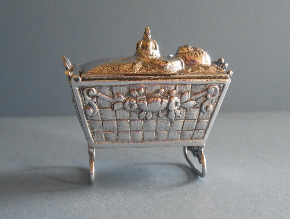 An Edwardian silver novelty snuff box crafted in the form of a miniature wicker cradle with a sleeping infant figure on the hinged lid.