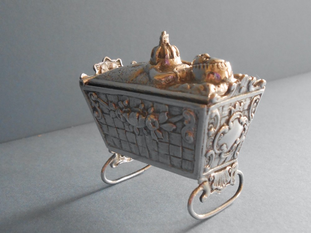 An Edwardian silver novelty snuff box crafted in the form of a miniature wicker cradle with a sleeping infant figure on the hinged lid. View X