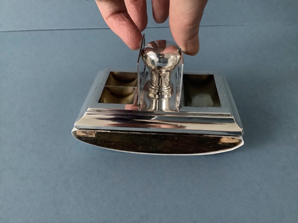 A rectangular silver desk rocker blotter featuring two hinged stamp compartments and a central rounded handle resting on a curved dark base. View III