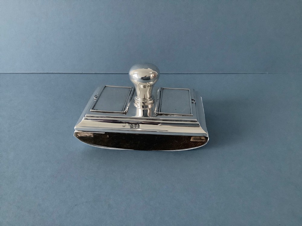 A rectangular silver desk rocker blotter featuring two hinged stamp compartments and a central rounded handle resting on a curved dark base. View VI