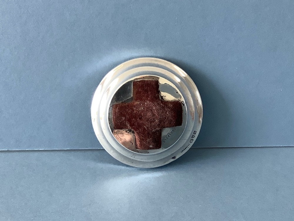 A circular hallmarked silver base set with a red cross-shaped velvet pin cushion at the centre.