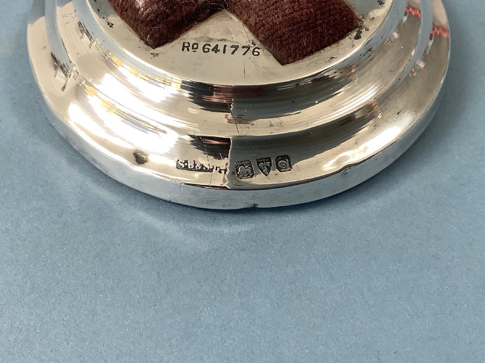 A circular hallmarked silver base set with a red cross-shaped velvet pin cushion at the centre. View II