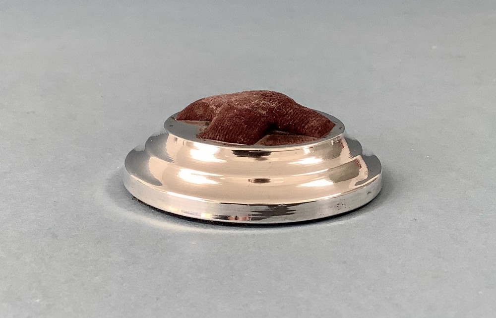 A circular hallmarked silver base set with a red cross-shaped velvet pin cushion at the centre. View III