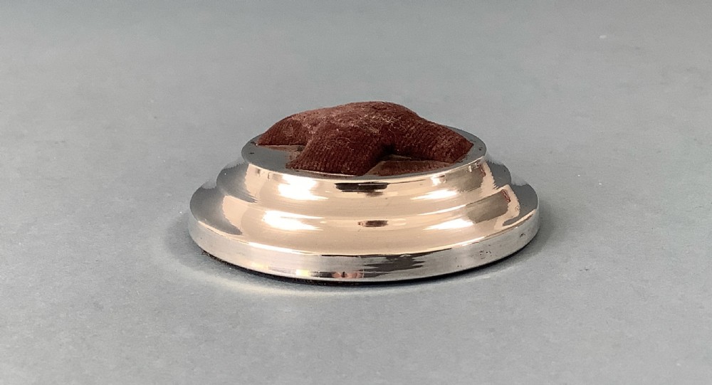 A circular hallmarked silver base set with a red cross-shaped velvet pin cushion at the centre. View VI