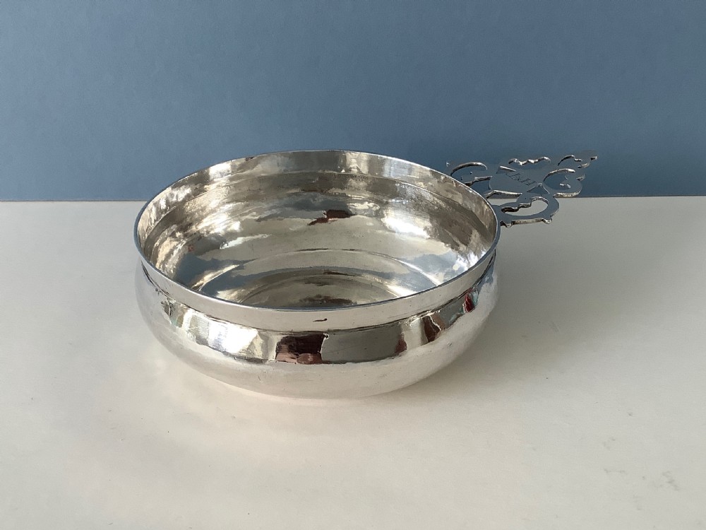 An early 18th-century Britannia standard silver bleeding bowl featuring a shallow round basin and a flat, geometrically pierced handle engraved with initials. View III