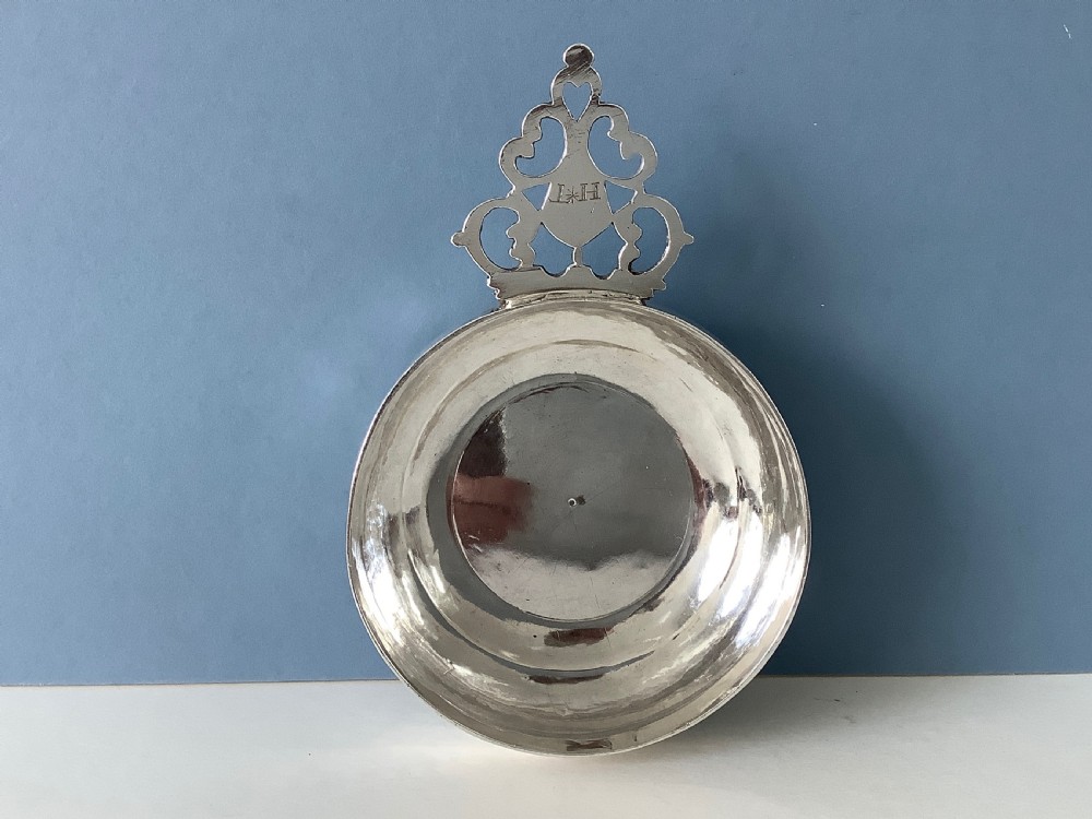 An early 18th-century Britannia standard silver bleeding bowl featuring a shallow round basin and a flat, geometrically pierced handle engraved with initials. View V