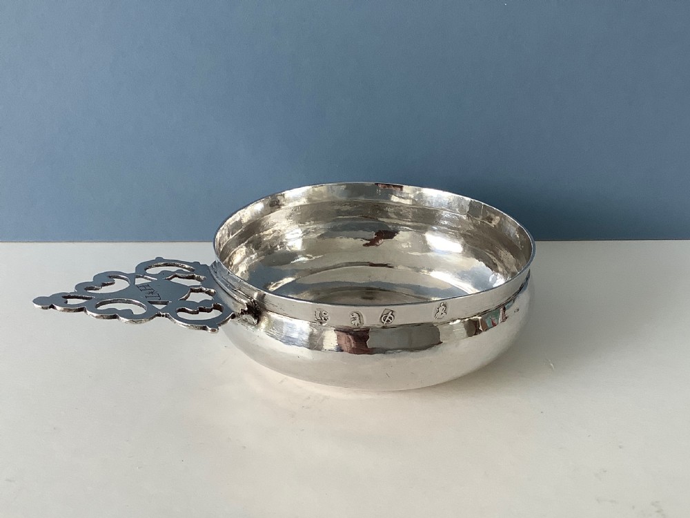 An early 18th-century Britannia standard silver bleeding bowl featuring a shallow round basin and a flat, geometrically pierced handle engraved with initials. View VII