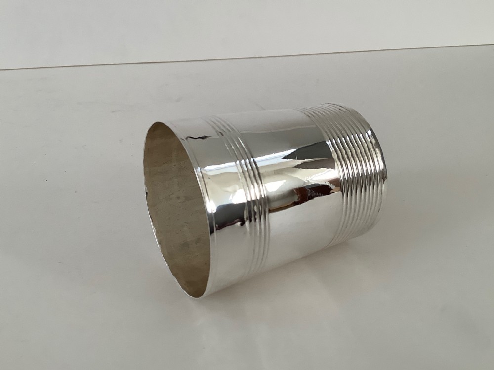 A cylindrical sterling silver beaker featuring horizontal reeded bands around the upper and lower exterior. View V