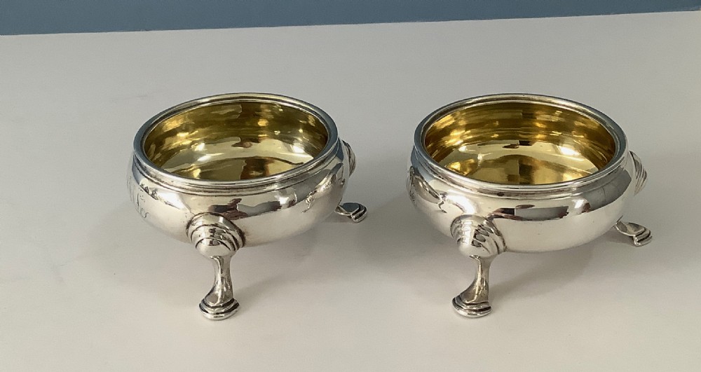 A pair of circular Georgian sterling silver open salt cellars featuring gilt interiors, engraved monograms, and tripod legs. View II