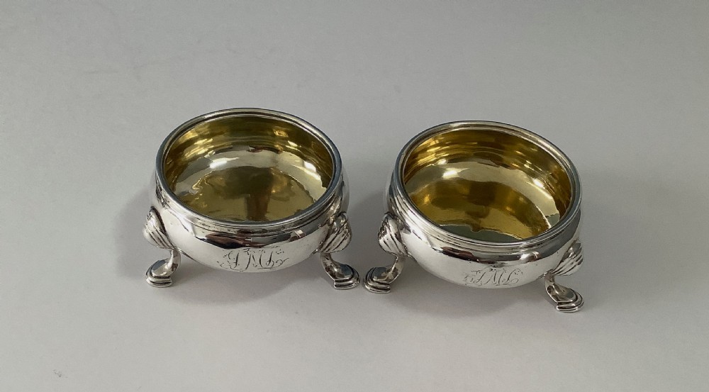 A pair of circular Georgian sterling silver open salt cellars featuring gilt interiors, engraved monograms, and tripod legs. View III