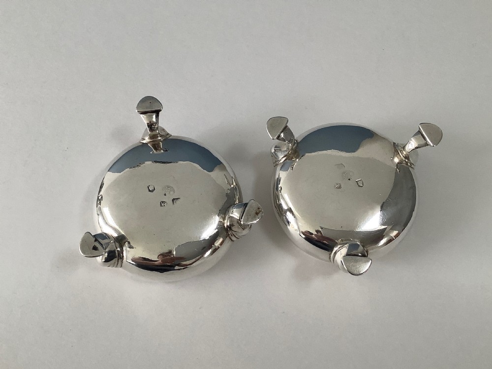A pair of circular Georgian sterling silver open salt cellars featuring gilt interiors, engraved monograms, and tripod legs. View VI