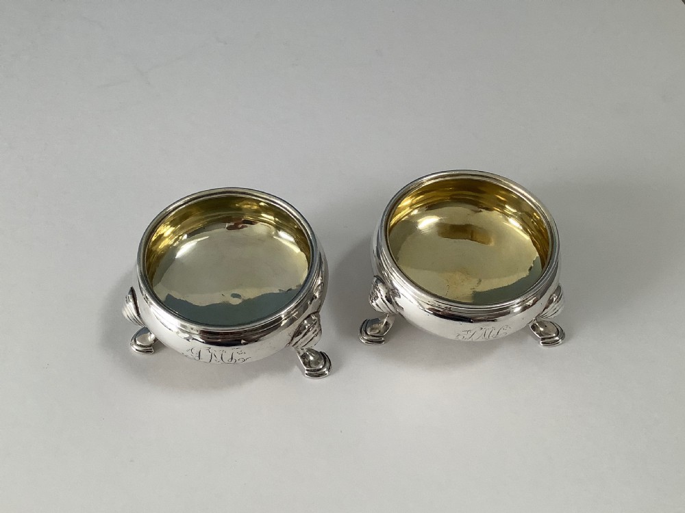 A pair of circular Georgian sterling silver open salt cellars featuring gilt interiors, engraved monograms, and tripod legs. View VII