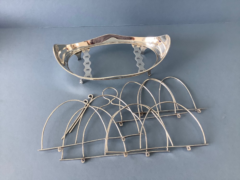 An antique Georgian silver toast rack with wire arch dividers displayed separately beside its footed oval frame.