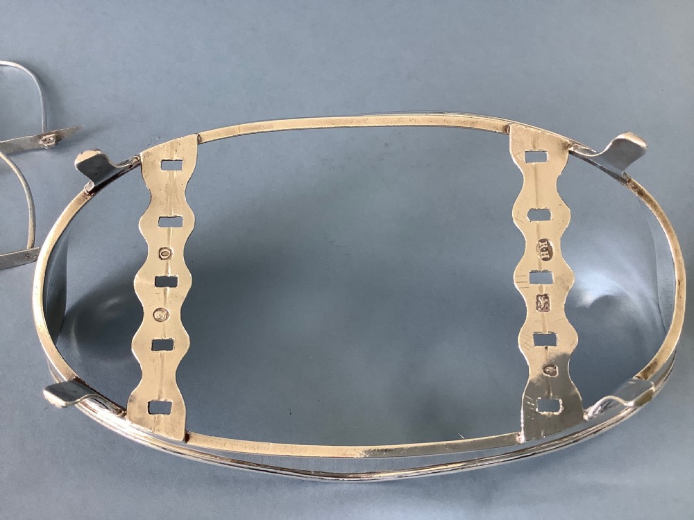 An antique Georgian silver toast rack with wire arch dividers displayed separately beside its footed oval frame. View II