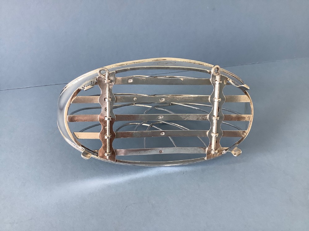 An antique Georgian silver toast rack with wire arch dividers displayed separately beside its footed oval frame. View III