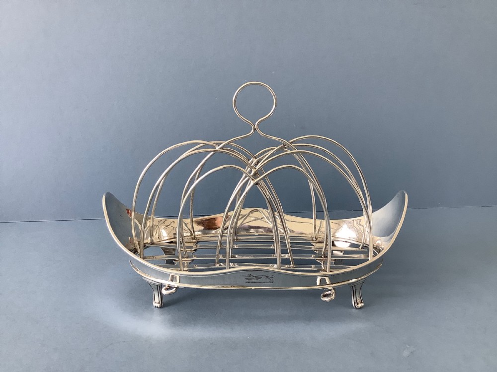 An antique Georgian silver toast rack with wire arch dividers displayed separately beside its footed oval frame. View V
