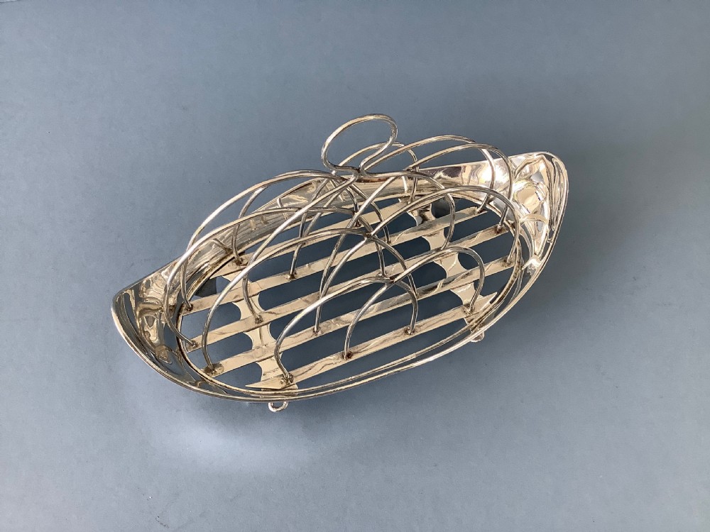 An antique Georgian silver toast rack with wire arch dividers displayed separately beside its footed oval frame. View VI