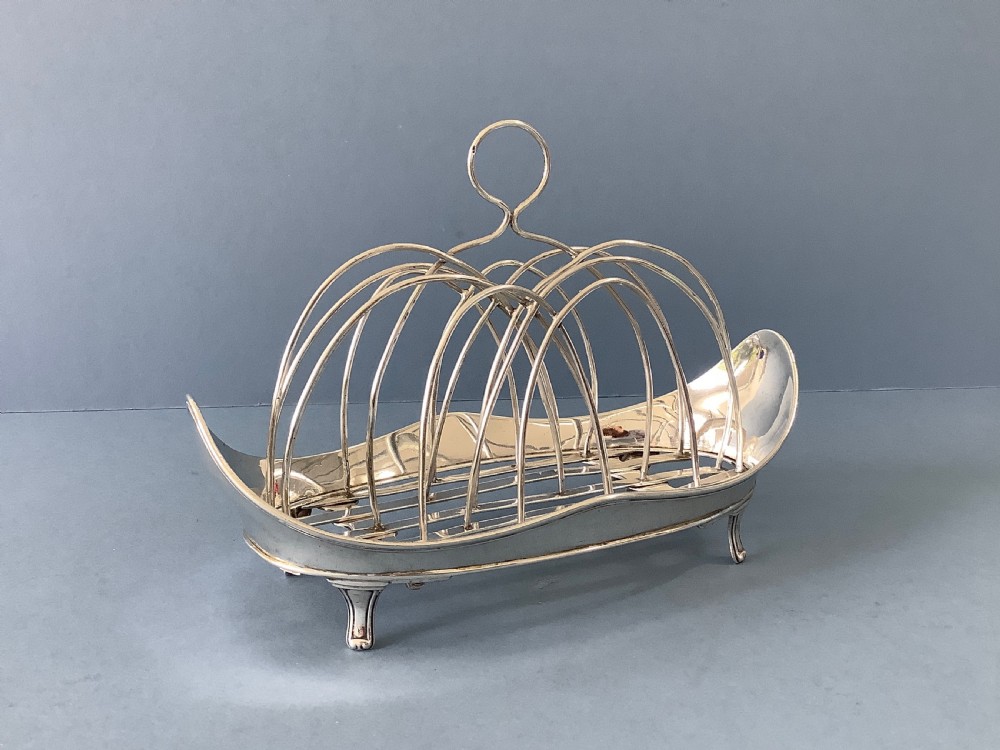 An antique Georgian silver toast rack with wire arch dividers displayed separately beside its footed oval frame. View VIII