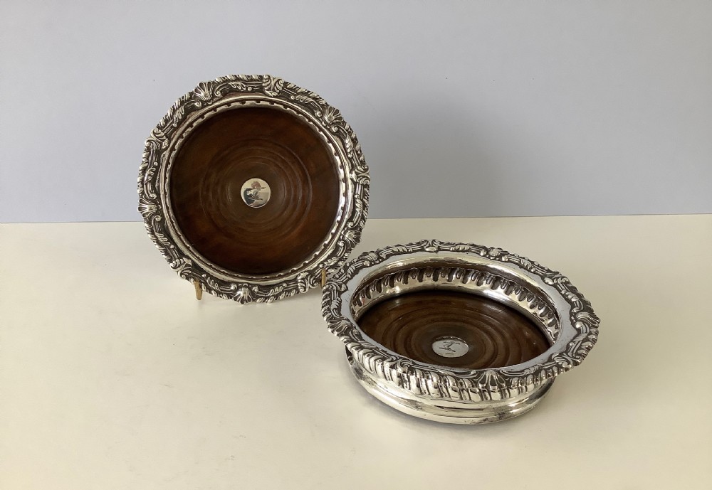 A pair of George III silver wine coasters featuring gadrooned rims with shell detailing, turned mahogany bases, and central silver bosses.