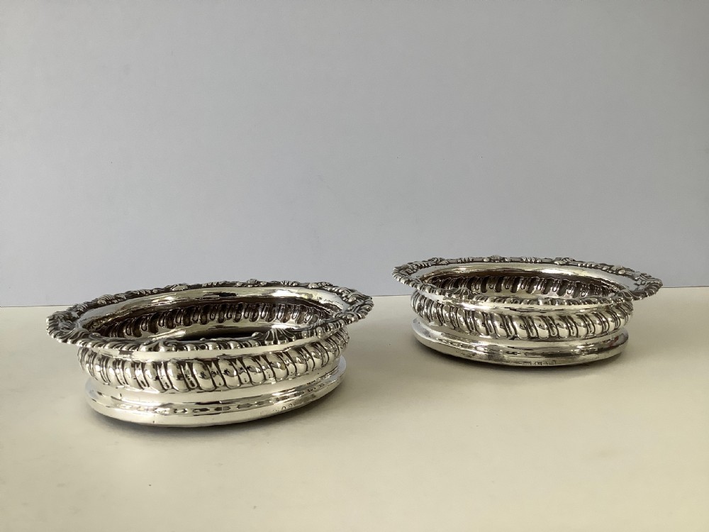 A pair of George III silver wine coasters featuring gadrooned rims with shell detailing, turned mahogany bases, and central silver bosses. View VII