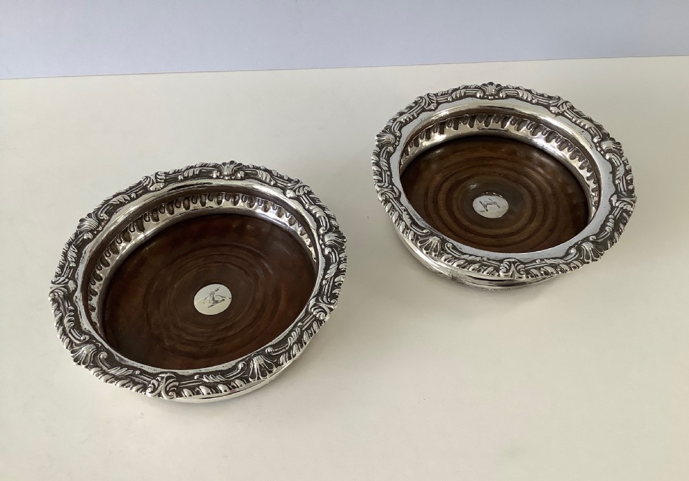 A pair of George III silver wine coasters featuring gadrooned rims with shell detailing, turned mahogany bases, and central silver bosses. View VIII