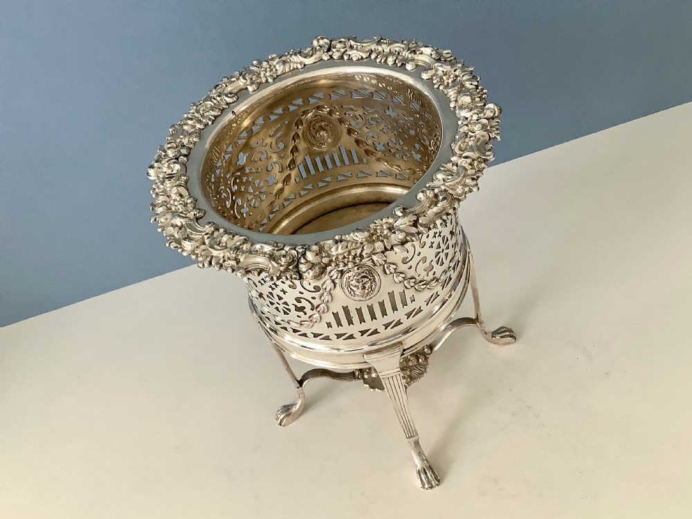 An antique silver-plated elevated wine coaster featuring pierced reticulated sides, a lion mask medallion, and tripod legs ending in claw feet. View V