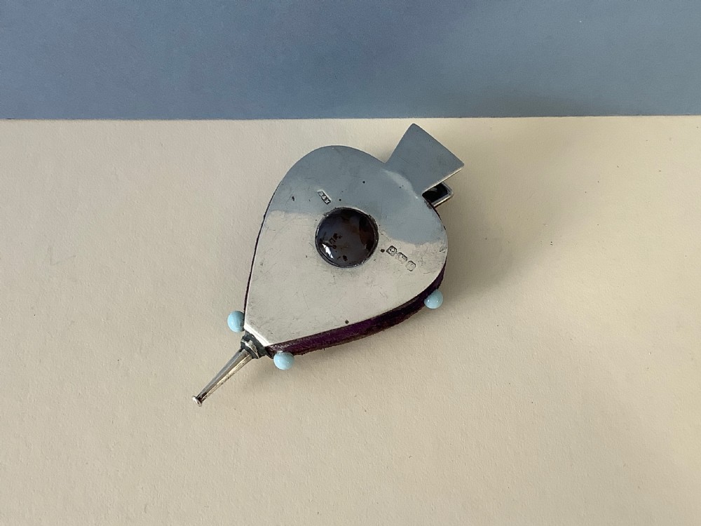 An Edwardian sterling silver pin cushion shaped as a pair of bellows with a central agate cabochon and a purple velvet core.