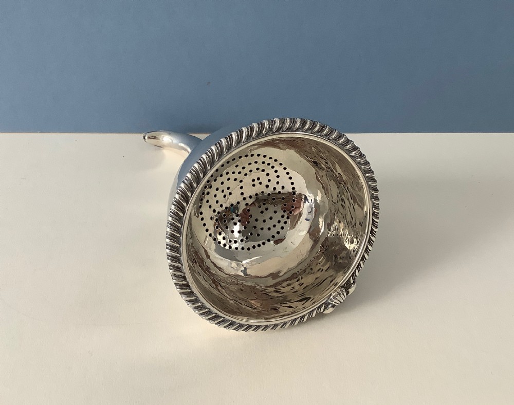 A three-part Georgian solid silver wine funnel featuring a perforated bowl with gadrooned rim, a retaining ring, and a curved spout. View II