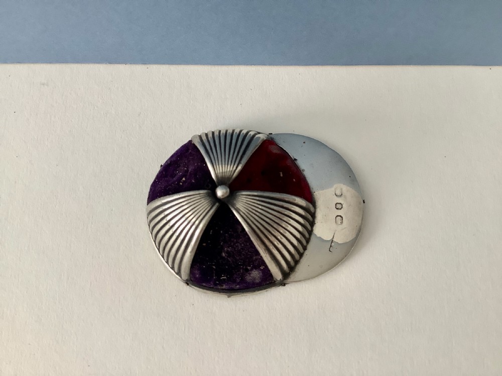 An antique silver pin cushion crafted in the form of a jockey cap with ribbed silver details, purple velvet fabric panels, and hallmarks stamped on the front brim. View V